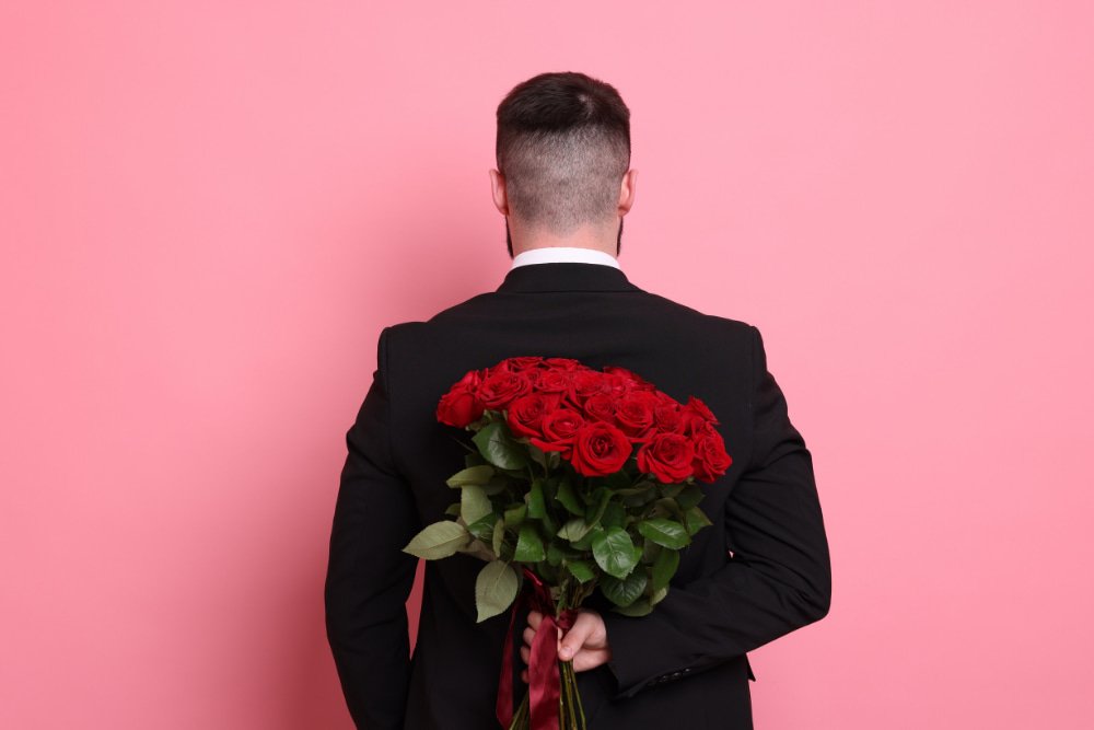 man hiding roses behind his back